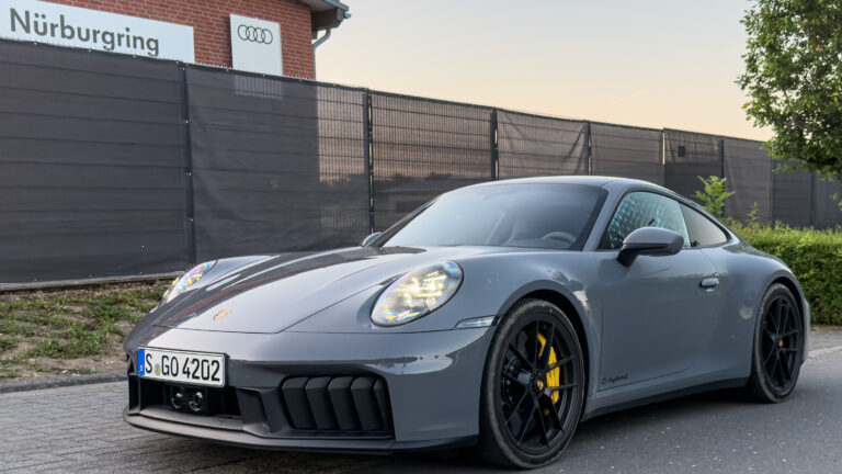 A grey Porsche 911 parked outside a building with an Audi logo and Nurburgring on the side.