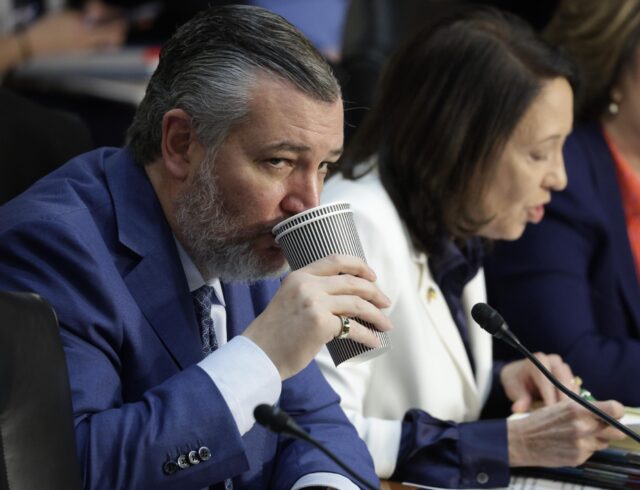 Sen. Ted Cruz drinks from a cup during a Senate committee hearing. Sen. Maria Cantwell sits next to him.