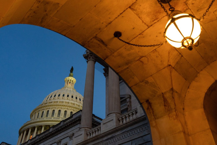The US Capitol dome at night, viewed from an archway.